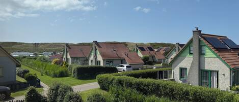 Une rangée de maisons aux toits inclinés, probablement équipées de panneaux solaires, se dresse dans un paysage verdoyant et vallonné.