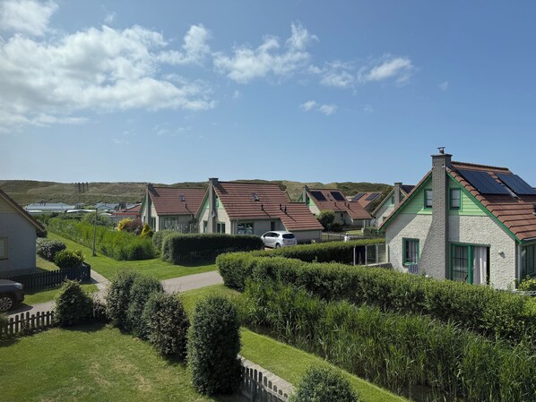 Une rangée de maisons aux toits inclinés, probablement équipées de panneaux solaires, se dresse dans un paysage verdoyant et vallonné.