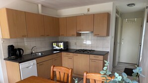 A compact kitchen with wooden cabinets, a Bosch dishwasher, a microwave, and a gas stove. - 3 bedroom accommodation in Julianadorp aan Zee (Julianadorp aan Zee)