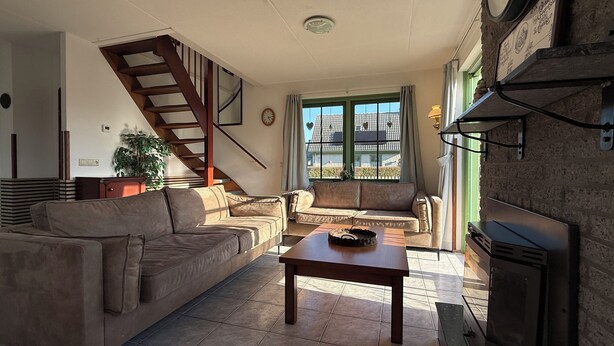 A living room with a sofa, a coffee table, a fireplace, a staircase, and a window with a view.