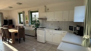 A compact kitchen with white cabinets, a stove, a sink, and a dining area with chairs and a table.