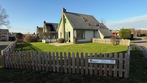 A single-story house with a sloped roof, a fenced yard, and a signboard in front.