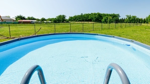 Ein klarer, blauer Pool mit einer Metallleiter, umgeben von einer Rasenfläche und einem Zaun.