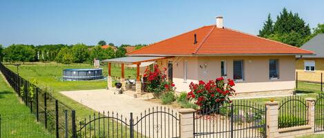 Une maison avec un toit rouge, un patio couvert et une cour clôturée.