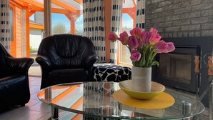 A modern living room with a glass coffee table, a black leather armchair, and a vase of pink tulips. - 3 bedroom accommodation in Julianadorp aan Zee (Julianadorp aan Zee)