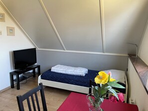 A small, modern bedroom with a bed, a TV, a desk, and a chair.