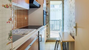 Una cocina compacta con armarios de madera, extractor de aire negro y un salpicadero con diseño. Se aprecia una pequeña mesa de comedor con taburetes.