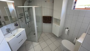 A modern bathroom with a glass-enclosed shower, white tiles, a white sink, and a toilet.