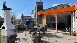 A patio area with a stone chimney, outdoor seating, and a view into a house with a glass door.