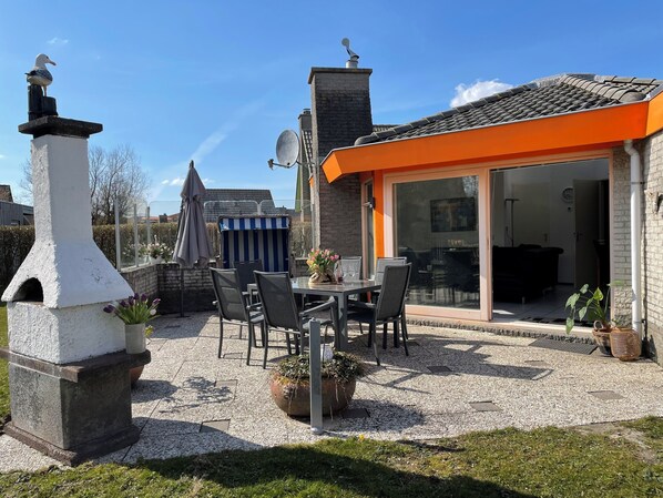 A patio area with a stone chimney, outdoor seating, and a view into a house with a glass door.