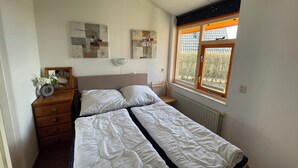 A bedroom with a bed, a dresser, a chair, and a window with a view of greenery.