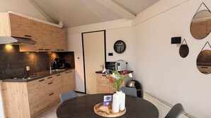 A modern kitchen with wooden cabinets, a stove, and a coffee maker. There is a dining table with chairs and a vase of flowers.