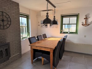 A dining area with a wooden table and black chairs, a brick wall, and a window with green frames.