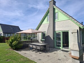 Een huis met een patio, compleet met een tafel, stoelen en een overdekte zithoek, en een groene deur.