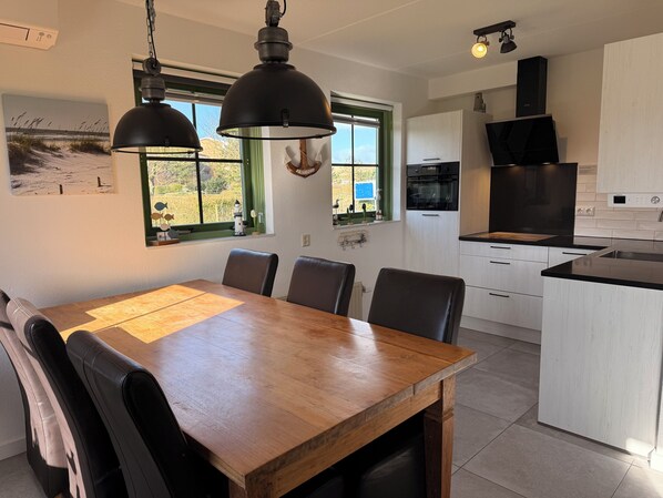 A modern kitchen with a central island, pendant lighting, and a dining area with a wooden table and chairs.
