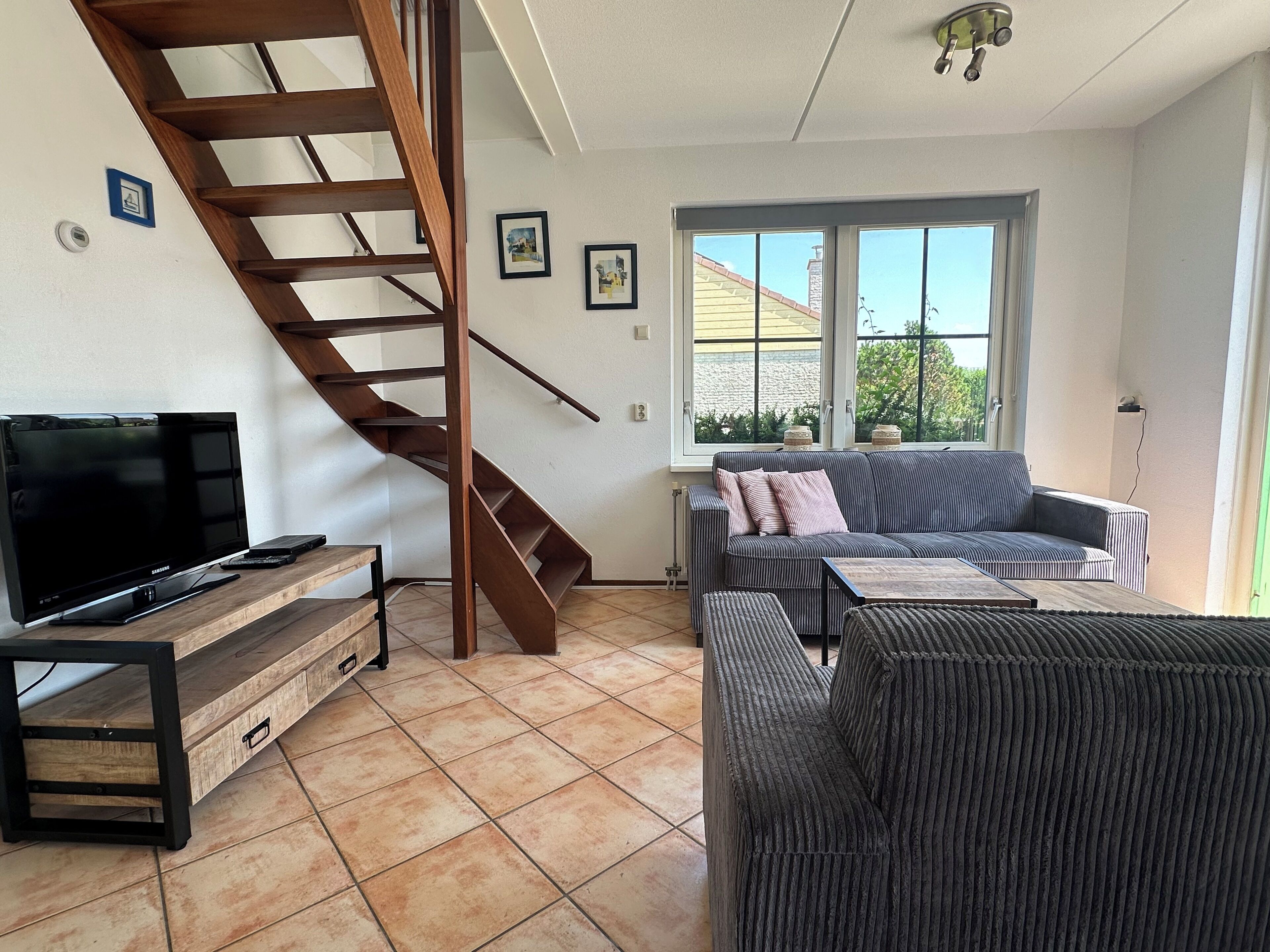 Un salon avec un escalier en bois, un téléviseur, un canapé et une fenêtre donnant sur une maison.