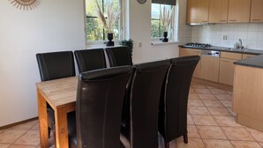 Una cucina con mobili in legno, un tavolo da pranzo con sedie, un orologio appeso al muro e finestre con piante.