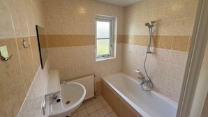 Un bagno con piastrelle beige, una finestra, un lavandino e una vasca da bagno.