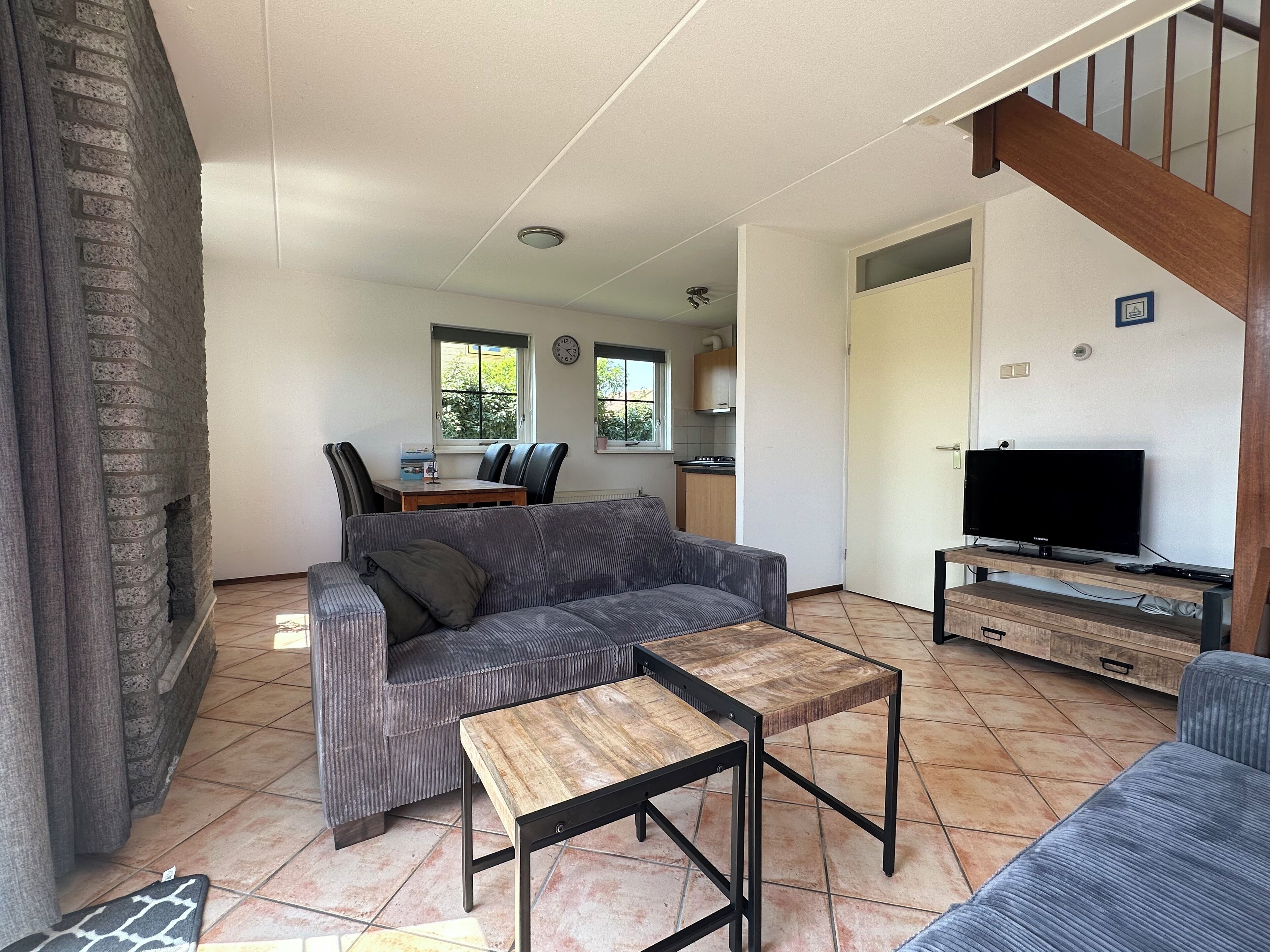 Een woonkamer met een bank, een salontafel, een televisie en een open haard. Achtergrond is een keuken.