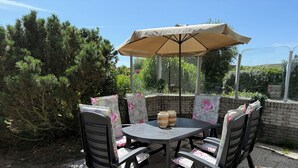 Una terrazza esterna con un tavolo rotondo, quattro sedie e un ombrellone grande.