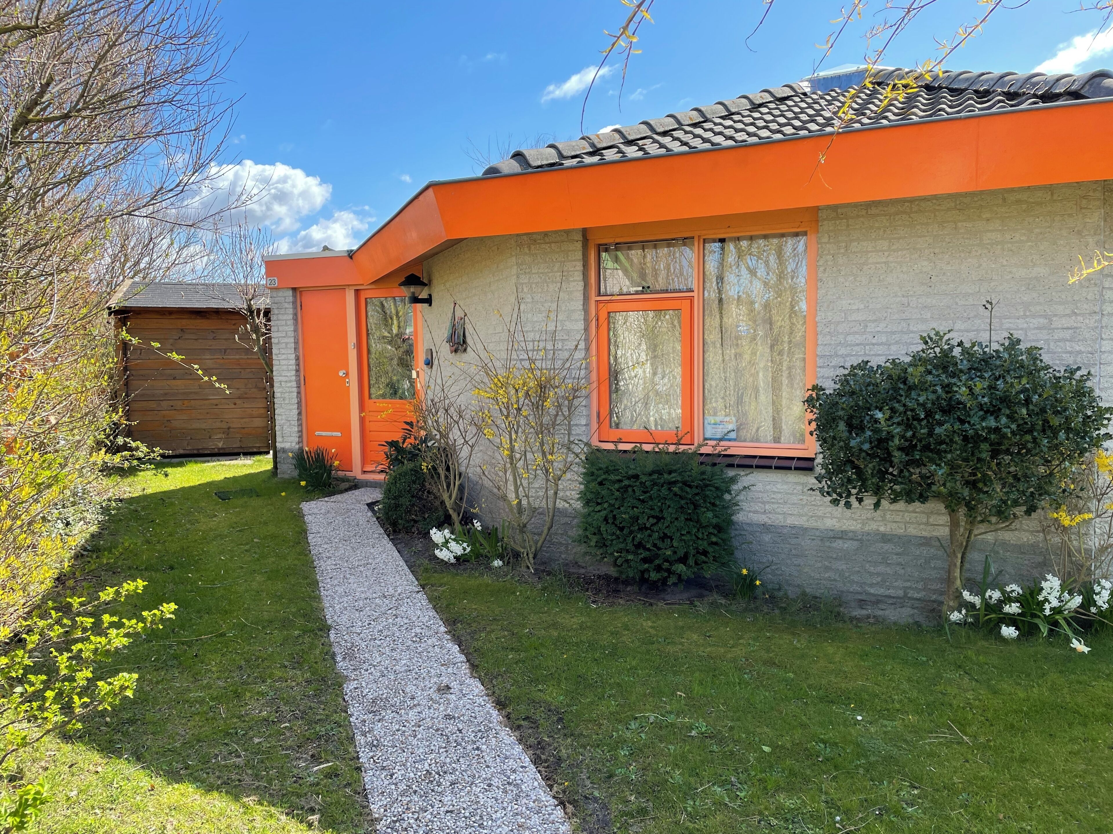 Een modern huis met een oranje gevel, een grindpad en een verzorgde tuin.