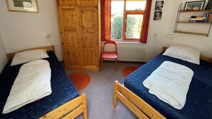 A bedroom with two single beds, a wooden wardrobe, a window with curtains, a radiator, and a small chair. - 3 bedroom accommodation in Julianadorp (Julianadorp)
