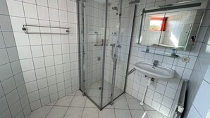 A modern bathroom with white tiled walls and floor, a glass shower enclosure, a white sink with a mirror above it, and a towel rack on the wall. - 3 bedroom accommodation in Julianadorp (Julianadorp)