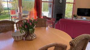 A cozy living room with a fireplace, large windows, and a dining area with wicker furniture. - 3 bedroom accommodation in Julianadorp (Julianadorp)