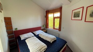 A bedroom with a bed, a window with curtains, a radiator, and a shelf with a lamp. - 3 bedroom accommodation in Julianadorp (Julianadorp)
