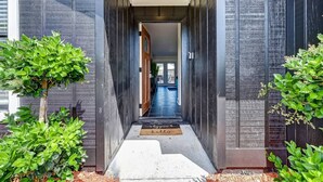 A modern building entrance with a dark facade, a clear pathway leading to the door, and green plants on either side. - NAS Jax Pool Hot-tub Gameroom Message for Spring (Jacksonville)