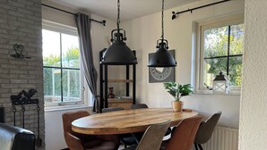 Un comedor con mesa y sillas de madera, una lámpara colgante y vistas al exterior con vegetación.
