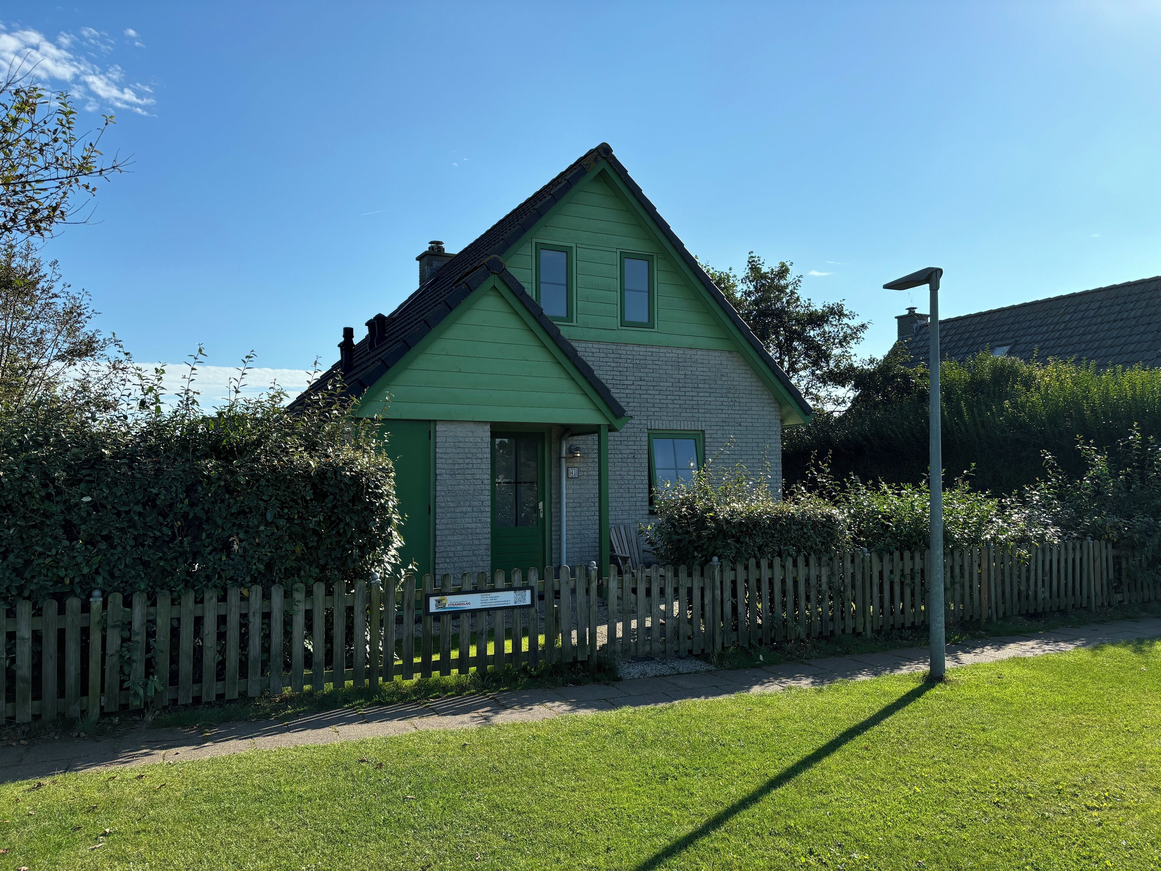 Une maison à deux étages, avec une façade verte et un petit porche à l’avant.