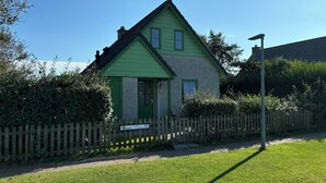 Una casa de dos pisos con fachada verde y un pequeño porche delantero.