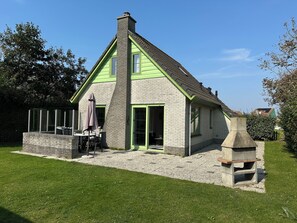 A house with a green roof, a chimney, and a patio with a table and chairs.