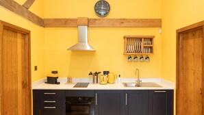 A kitchen with wooden cabinets, a stainless steel range hood, a yellow wall, a clock, and a knife rack. - Jossies Snug - peaceful, private garden/hot tub, swimming lake, Spa and Wellness (Bletchingley)