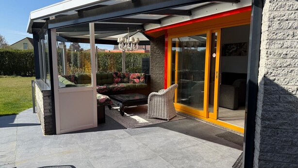 An outdoor patio area with a covered seating area, a stone wall, and a glass door leading to an interior space. - 3 bedroom accommodation in Julianadorp aan Zee (Julianadorp aan Zee)