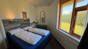 A bedroom with a double bed, a nightstand, a mirror, and a window with a view of greenery. - 3 bedroom accommodation in Julianadorp aan Zee (Julianadorp aan Zee)