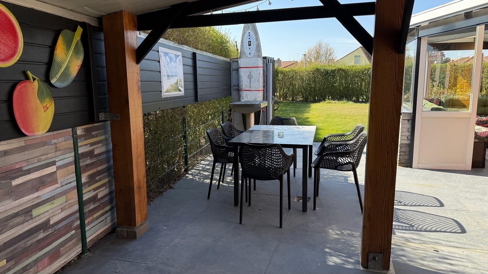 Patio esterno con tavolo e sedie, recinzione in legno e vista sul giardino.