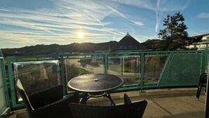 Ein Balkon mit Tisch und Stühlen, der auf eine Straße und Gebäude mit blauem Himmel und Sonne blickt.