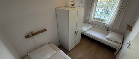 Ein kleiner, sauberer Raum mit einem Bett, einem Kleiderschrank und einem Fenster mit Ausblick.