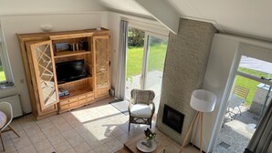 Een moderne woonkamer met een televisie, een houten kast, een rieten stoel en een open haard.