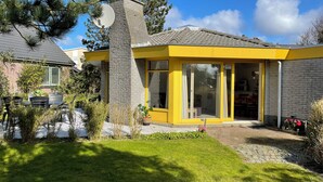 Una casa con fachada amarilla, una chimenea de ladrillo y una puerta de cristal que da a un espacio interior.