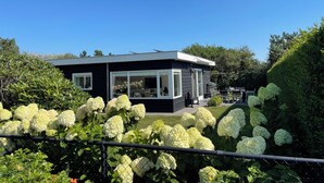 Ein modernes Haus mit großen Fenstern, umgeben von üppiger Bepflanzung und weißen Hortensienbüschen.