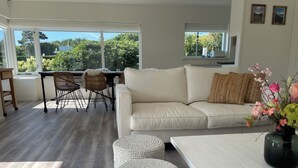 Ein modernes Wohnzimmer mit einer Couch, Poufs und einem Essbereich mit Stühlen und einem Tisch.