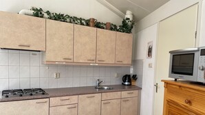 Cucina con mobili color beige, piano cottura a gas, lavello e forno a microonde su un mobiletto in legno.