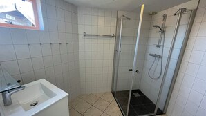 Un bagno con cabina doccia in vetro, lavandino bianco e pavimento piastrellato.