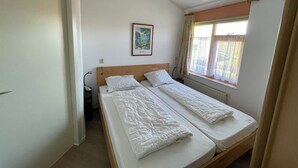 Una stanza piccola e pulita con due letti singoli, una finestra con tende e un quadro appeso al muro.