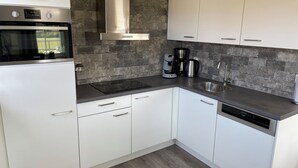 A modern kitchen with white cabinets, a stainless steel range hood, a built-in oven, a coffee maker, and a dishwasher.