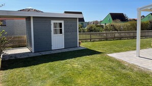 A small, single-story building with a white door and windows, surrounded by a well-maintained lawn and a wooden fence.