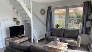 A modern living room with a grey sofa, a flat-screen TV, a coffee table, and a staircase.